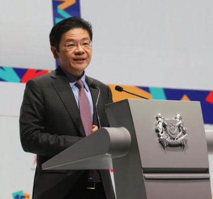 Lawrence Wong, Singapore's fourth Prime Minister, speaks at a podium during his swearing-in ceremony, surrounded by government officials and supporters.