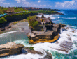 Tanah Lot Temple in Bali perched on a rocky outcrop during sunset with ocean waves below.