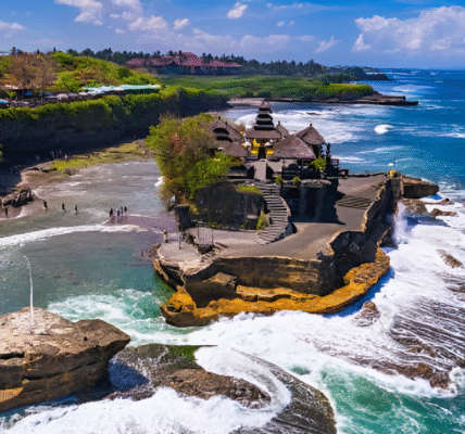 Tanah Lot Temple in Bali perched on a rocky outcrop during sunset with ocean waves below.