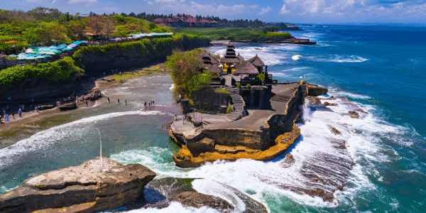 Tanah Lot Temple in Bali perched on a rocky outcrop during sunset with ocean waves below.